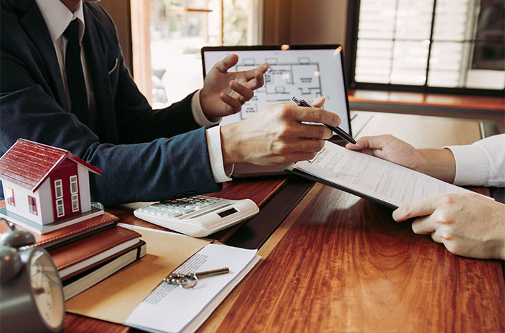 real-estate-home-are-pointing-to-insurance-contrac-2021-09-03-01-48-34-utc.jpg Business people discussing real estate at at a table with a blueprint in the background