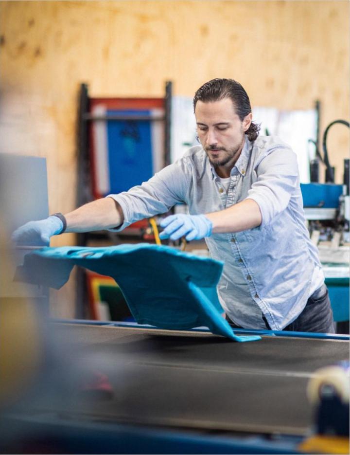 Photo of a man working on a tee-shirt in a clothing factory
