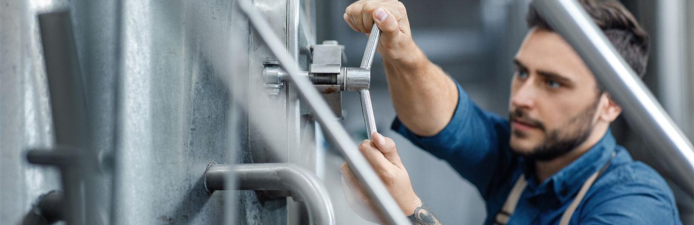 management-of-equipment-at-brewery-and-control-man-2021-08-29-23-19-12-utc.jpg A man working in a brewery is turning a handle